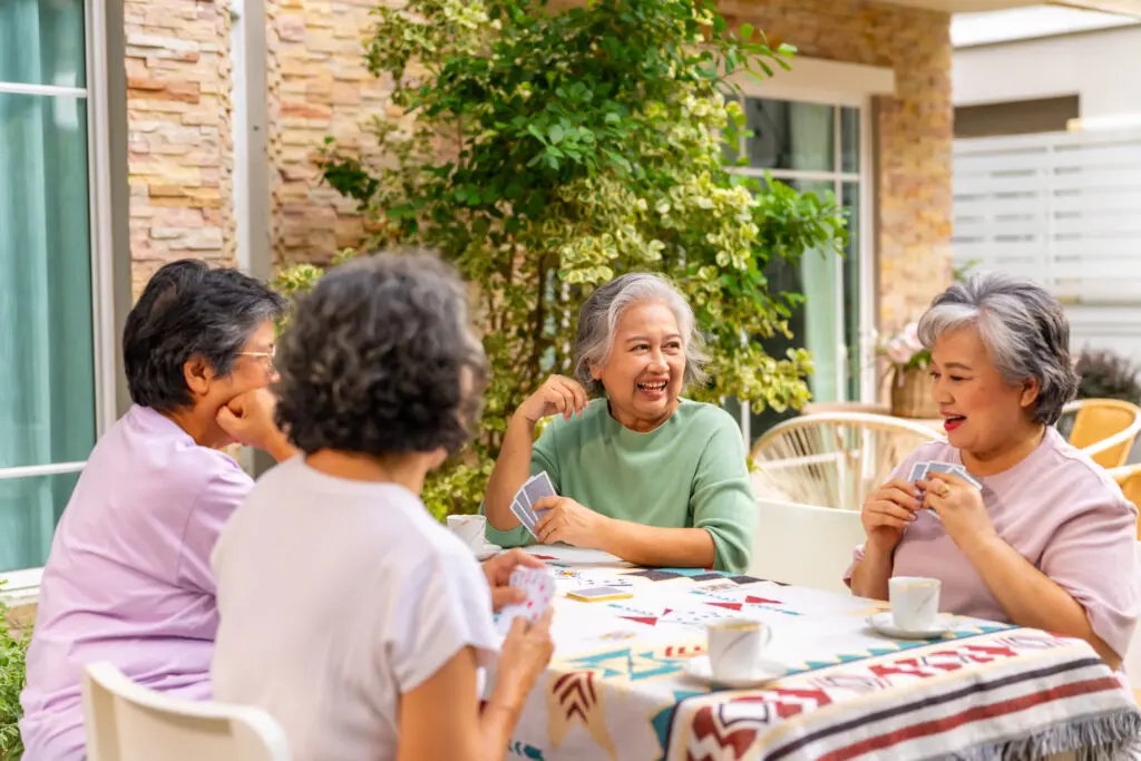 four senior asian women playing cards in their some at The Arlington Of Naples, a dementia care community in Naples, Florida.
