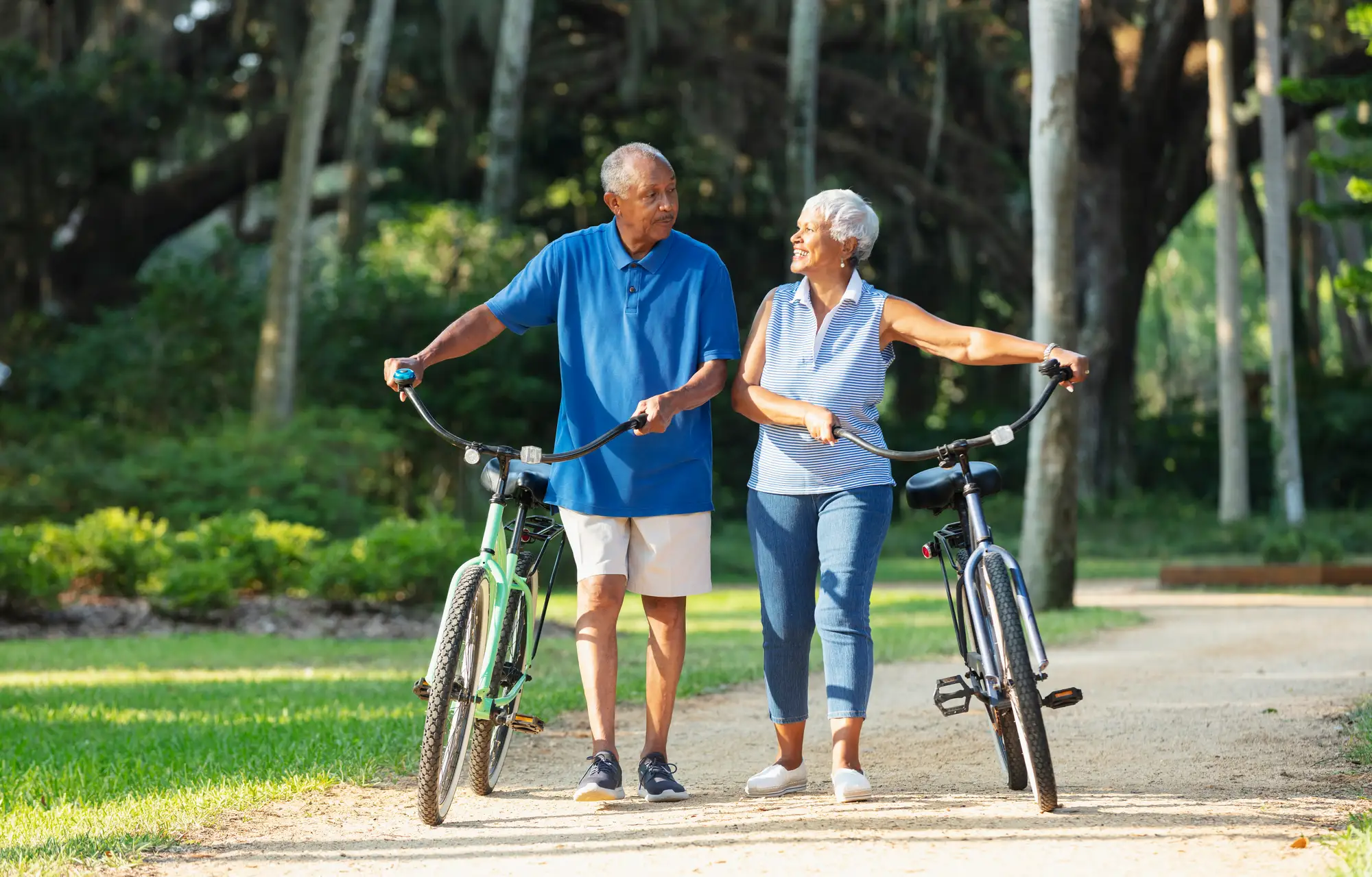 Two seniors walking their bikes along a path