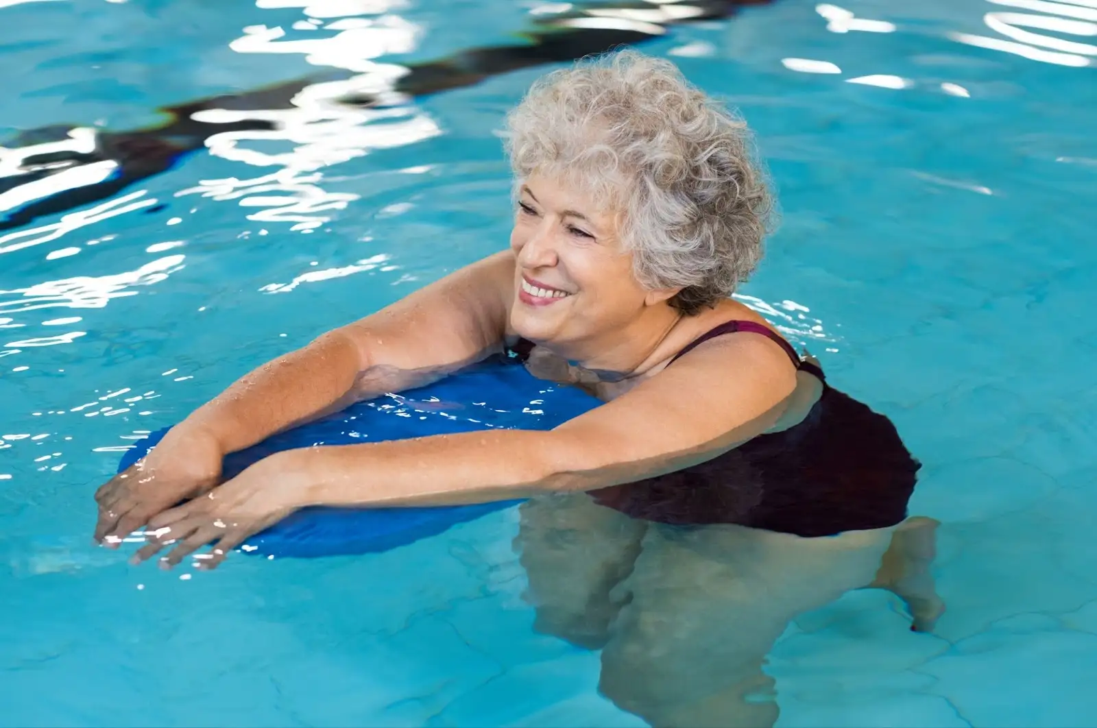 Resident of The Arlington of Naples enjoying active pool exercises for seniors. She is doing flutter kicks.