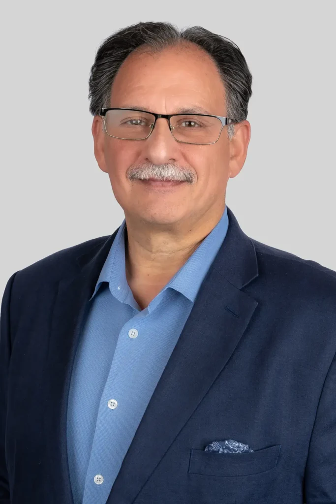 Man with glasses, mustache, graying hair in blue suit and light blue shirt by The Arlington Of Naples, facing forward.